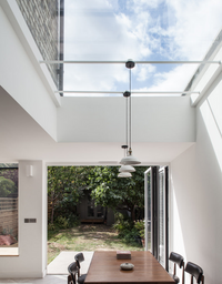 flat rooflight installed in a kitchen with white lights dangling from it over a wooden table. doors lead to the garden